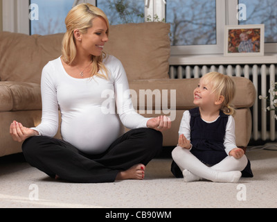 Glückliche schwangere Mutter und ihre kleine Tochter gemeinsam Spaß haben beim Yoga zu Hause Stockfoto