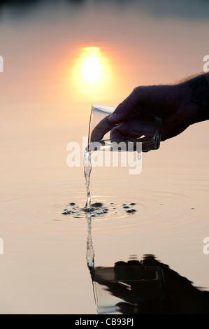 Gießen Wasser aus einem Glas zu einem noch See bei Sonnenaufgang in Indien. Silhouette Stockfoto