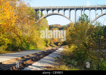 Ein Personenzug runden einen Bogen und nähert sich unter eine hohe Bogenbrücke in einer landschaftlich reizvollen Gegend Stockfoto