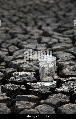Prickelndes Glas Wasser auf trockene rissige Erde Stockfoto
