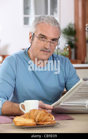 Im mittleren Alter Mann liest Zeitung beim Frühstück Essen Stockfoto