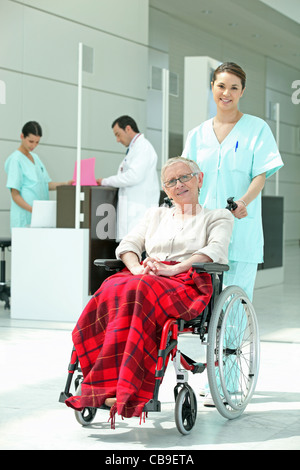 Krankenschwester, eine ältere Frau in einem Rollstuhl schieben Stockfoto