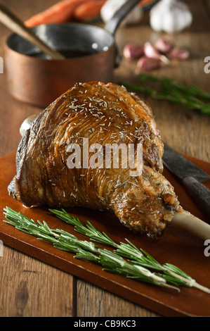 Gebratene Lammkeule mit Knoblauch und Rosmarin auf einem Schneidebrett Stockfoto