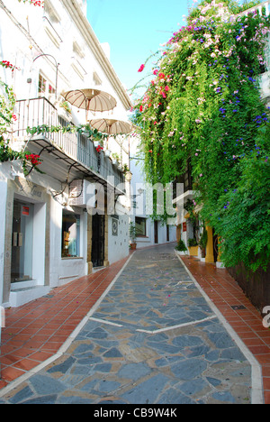 Eine schöne Straße in Marbella, Spanien, hat Crazy Pflaster, eine Fülle von schönen Blumen und Sonnenschirme auf dem Balkon. Stockfoto