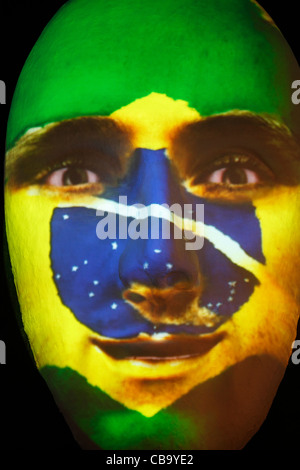 Riesige Skulptur eines Gesichts beleuchtet durch ein Bild von einem brasilianischen Fahne bemaltem Gesicht während des Festival of lights 2011 in Berlin Stockfoto