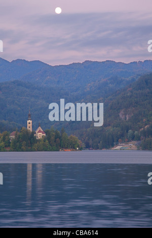 Mond Einstellung bei Sonnenaufgang über Hügel und Insel-Kirche am See Bled, Slowenien. Stockfoto