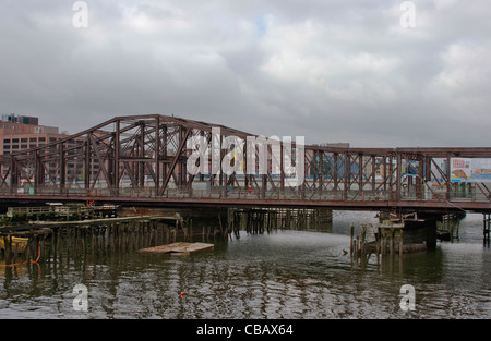 rostige alte Fußgängerbrücke über den Hafen von Boston mit hölzernen Pfählen und Gebäuden im Hintergrund, bewölkt Stockfoto