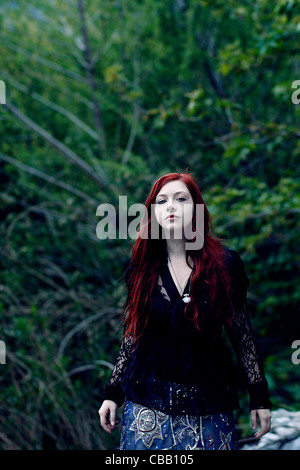 Ein Mädchen mit roten Haaren allein im Wald mit Bäumen hinter ihr Stockfoto