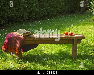 Eine entspannte Atmosphäre in einem sonnigen Land-Garten - hat die Holzbank, ein Buch, Decke und Erfrischungen auf Sie Stockfoto