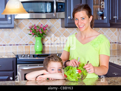 Schöne Mutter und Sohn mischen einen Salat in der Küche Stockfoto