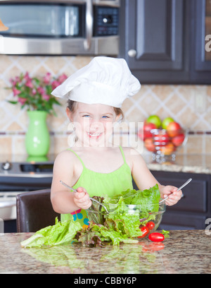 Niedliche kleine Mädchen spielen mit einer Schüssel Salat Stockfoto