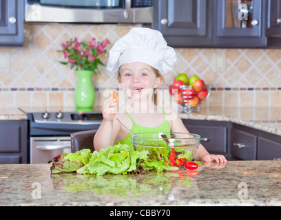 Niedliche kleine Mädchen spielen mit einer Schüssel Salat Stockfoto