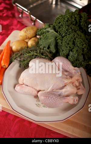 Rohe ganzes Huhn auf ein Schneidebrett mit Kräutern und Gemüse Stockfoto