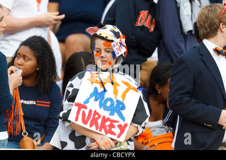 Weibliche Virginia Cavaliers Fan auf der Tribüne, gekleidet wie eine Kuh mit einem Schild, das Essen Mor Türkei vor dem Spiel Virginia Tech Hokies im Scott Stadium, Charlottesville, Virginia, Vereinigte Staaten von Amerika liest Stockfoto