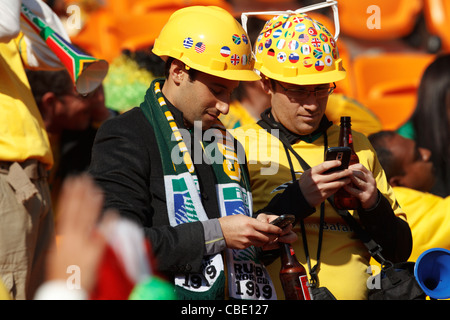 Beim Eröffnungsspiel der FIFA Fussball-Weltmeisterschaft zwischen Südafrika und Mexiko am 11. Juni 2010 im Soccer City Stadium in Johannesburg, Südafrika, schauen zwei Fußballfans ihre Mobilgeräte. Nur redaktionelle Verwendung. Kommerzielle Nutzung verboten. Keine Nutzung von Push-to-Mobilgeräten. (Foto: Jonathan Paul Larsen / Diadem Images) Stockfoto