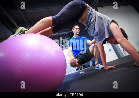 Junge Asiatin wird von personal Trainer dabei Liegestütze auf einer Yoga-Ball trainiert. Stockfoto