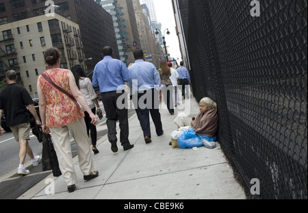 Ältere Obdachlose sitzen auf dem Bürgersteig entlang 8th Avenue in New York City als die Welt ihr vergeht. Stockfoto