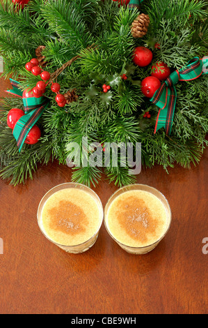 Draufsicht auf zwei Gläser Eierlikör, garniert mit Muskatnuss auf einem Holztisch mit einem dekorativen Weihnachtskranz Stockfoto