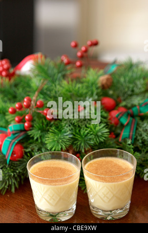 Zwei Kristallgläser von Eierlikör, garniert mit Muskatnuss und eine dekorative Adventskranz. Stockfoto