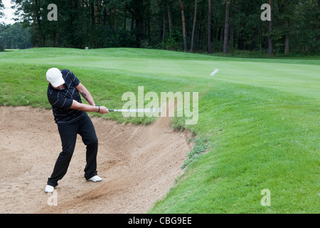 Ein Golfer, die Kollision mit einem Ball aus einem Sandfang Stockfoto
