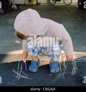 Ein kleiner Junge auf dem Bürgersteig mit Kreide kritzeln Stockfoto