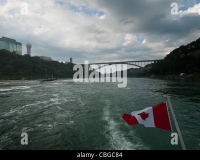 Die kanadische Flagge flattert von hinten von einem Ausflugsboot mit Niagara Falls im Hintergrund. Stockfoto