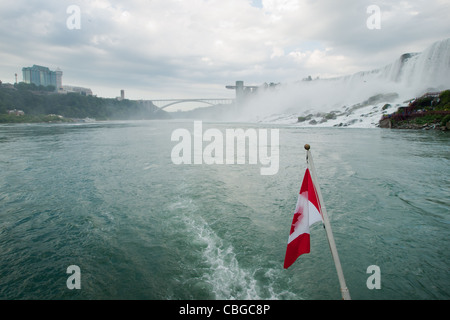 Die kanadische Flagge flattert von hinten von einem Ausflugsboot mit Niagara Falls im Hintergrund. Stockfoto