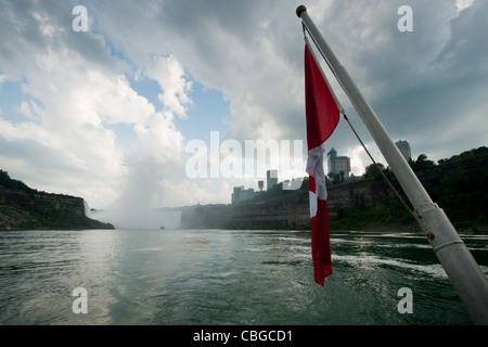 Die kanadische Flagge flattert von hinten von einem Ausflugsboot mit Niagara Falls im Hintergrund. Stockfoto