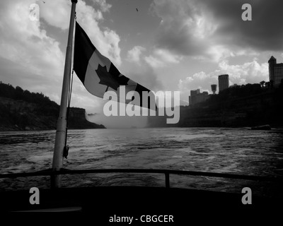 Die kanadische Flagge flattert von hinten von einem Ausflugsboot mit Niagara Falls im Hintergrund. Stockfoto