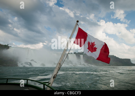 Die kanadische Flagge flattert von hinten von einem Ausflugsboot mit Niagara Falls im Hintergrund. Stockfoto