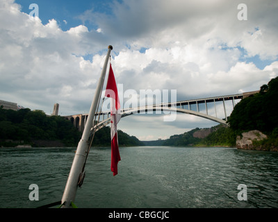 Die kanadische Flagge flattert von hinten von einem Ausflugsboot mit Niagara Falls im Hintergrund. Stockfoto