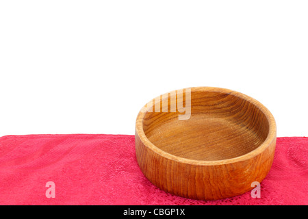 Leere Teak Holz Schüssel auf einer roten Platz-Matte isoliert auf einem weißen Hintergrund. Kleine Runde Holzschale close-up auf einem roten Tuch Tischset vor weiß. Stockfoto