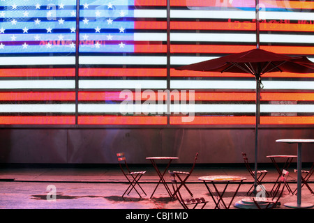 Leere Tische und Sonnenschirm vor beleuchtet Stars & Stripes, USA Flagge, Times Square, New York City, NY, USA Stockfoto