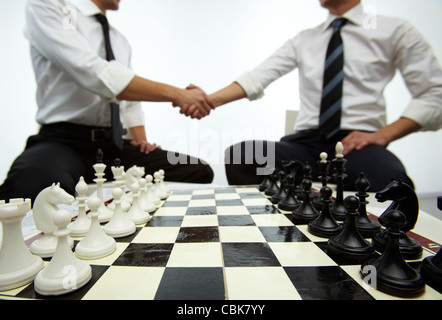 Vier Reihen von Schach Figuren am Schachbrett mit zwei Männern Handshaking auf Hintergrund Stockfoto