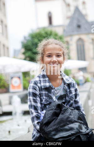 Lächelnd junges Mädchen sitzt am Brunnen im Thomaskirchhof vor St. Thomaskirche in Leipzig, Sachsen, Deutschland Stockfoto