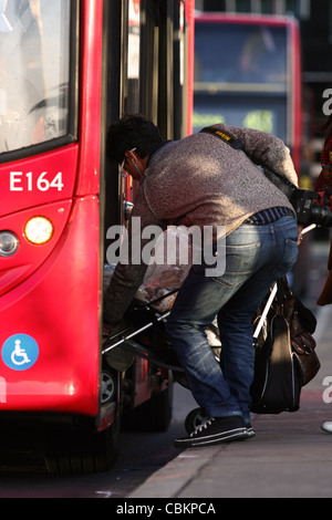 zwei Menschen, die kämpfen, um zu einen roten Londoner Bus mit einem Kinderwagen an Bord Stockfoto