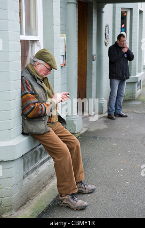 Älterer Mann SMS auf Handy saß auf der Fensterbank vor Pub in Kington Herefordshire England UK Stockfoto