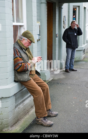 Älterer Mann SMS auf Handy saß auf der Fensterbank vor Pub in Kington Herefordshire England UK Stockfoto