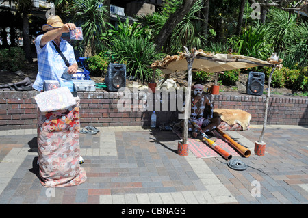 Ein Aborigine-Straßenmusiker spielt sein Didgeridoo vor seiner Schlange am Circular Quay in Sydney, New South Wales, Australien Stockfoto