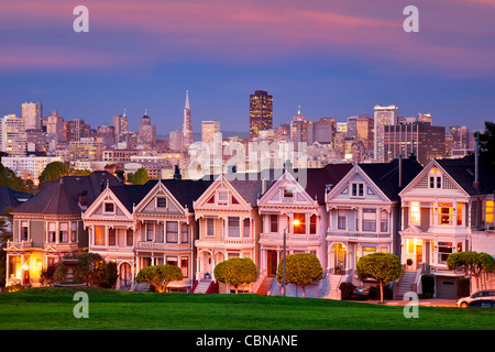 Viktorianische Häuser - die "Painted Ladies" von San Francisco mit der Skyline darüber hinaus in der Dämmerung. Stockfoto