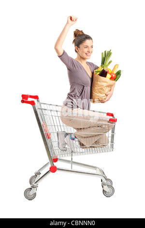 Eine glückliche Frau mit einer Papiertüte posiert in einem Einkaufswagen isoliert auf weißem Hintergrund Stockfoto