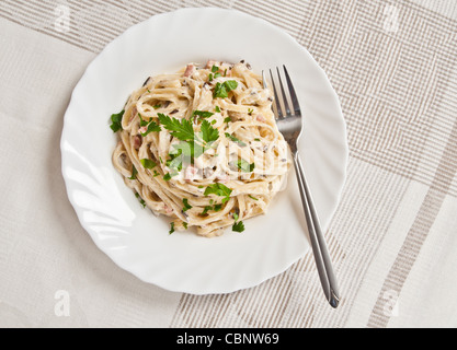 Spaghetti. Fettuccine Carbonara in einer weißen Schüssel, garniert mit Speck, Champignons und Petersilie. Cremige Soße. Stockfoto