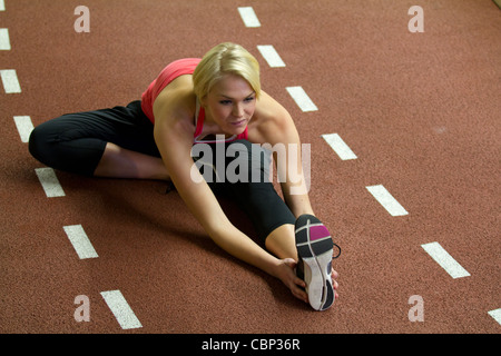 Junge Frau mit kurzen blonden Erben in rotes Top streckt sich vor der Ausführung Stockfoto