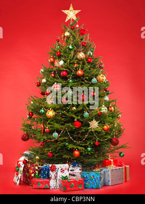 Schöner geschmückter Weihnachtsbaum mit bunten verpackt Geschenke unter ihm. Auf hellen roten Hintergrund isoliert. Stockfoto