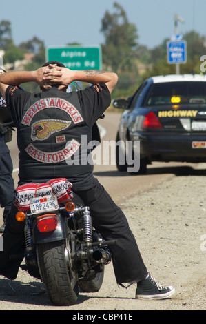 Ein Mitglied der Hells Angels hält seine Hände hinter seinem Kopf während einer Verkehrskontrolle. Stockfoto