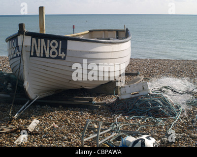 Kleines Boot zum Angeln verwendet gezogen auf einem steinigen Strand mit Netzen und anderen Utensilien, die an den Strand gelegt, Südküste Englands, Bexhill Stockfoto