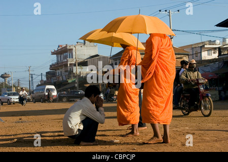 Buddhistische Mönche stehen während des Empfangs Reis von einem Mann in Ban Lung, Kambodscha auf einer unbefestigten Straße. Stockfoto