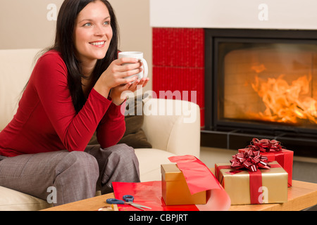 Glückliche Frau einwickeln Weihnachtsgeschenk Kamin genießen Heißgetränk Stockfoto