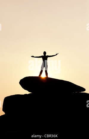 Indischer Mann auf einem Felsen umarmt die Sonne steht. Silhouette. Indien Stockfoto