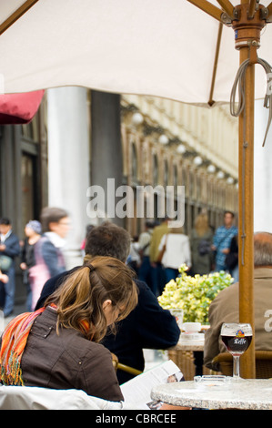 Vertikale Nahaufnahme einer Frau eine Zeitschrift liest und haben ein Leffe-Bier in einem Straßencafé. Stockfoto